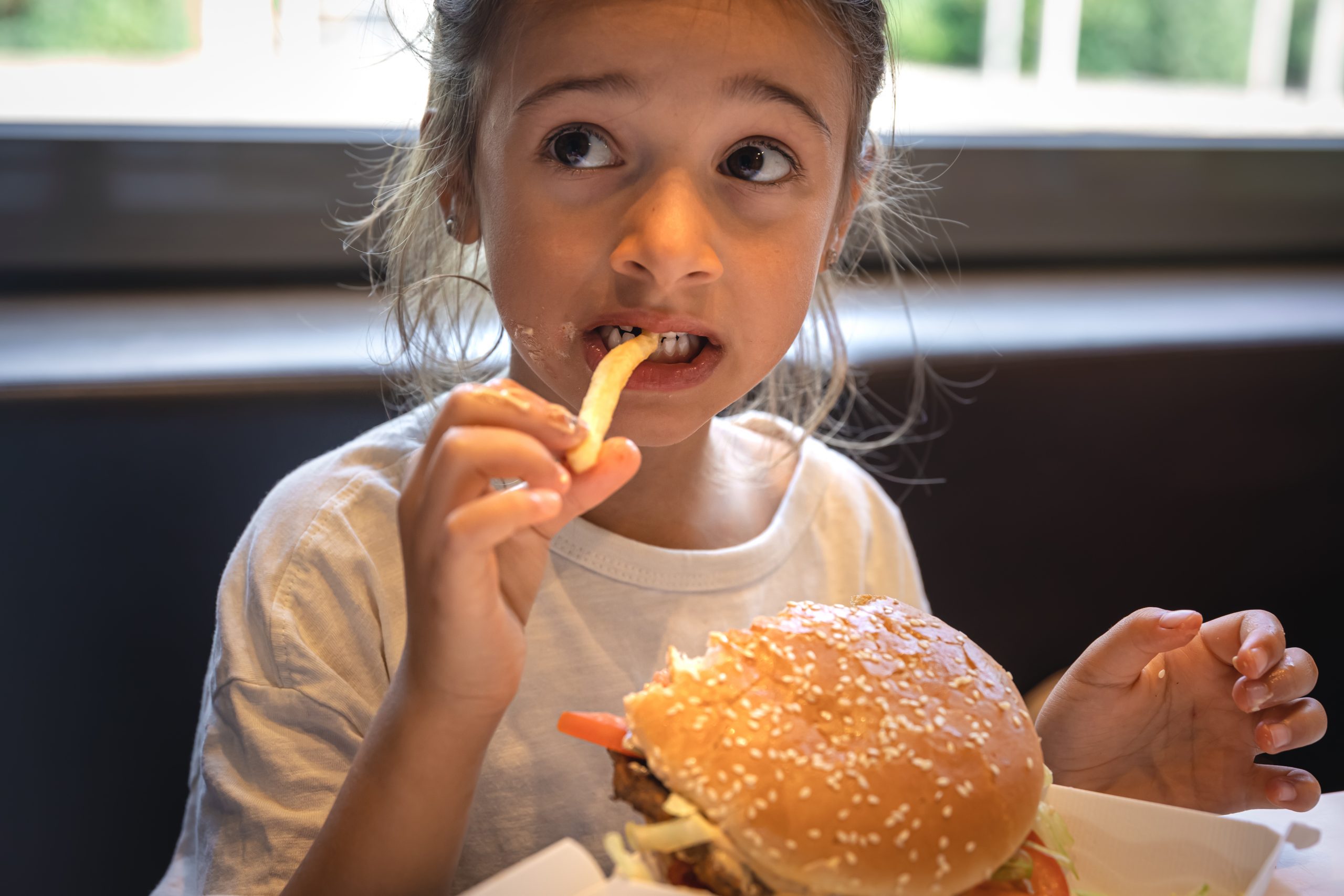 A little girl eats fast food in a cafe.