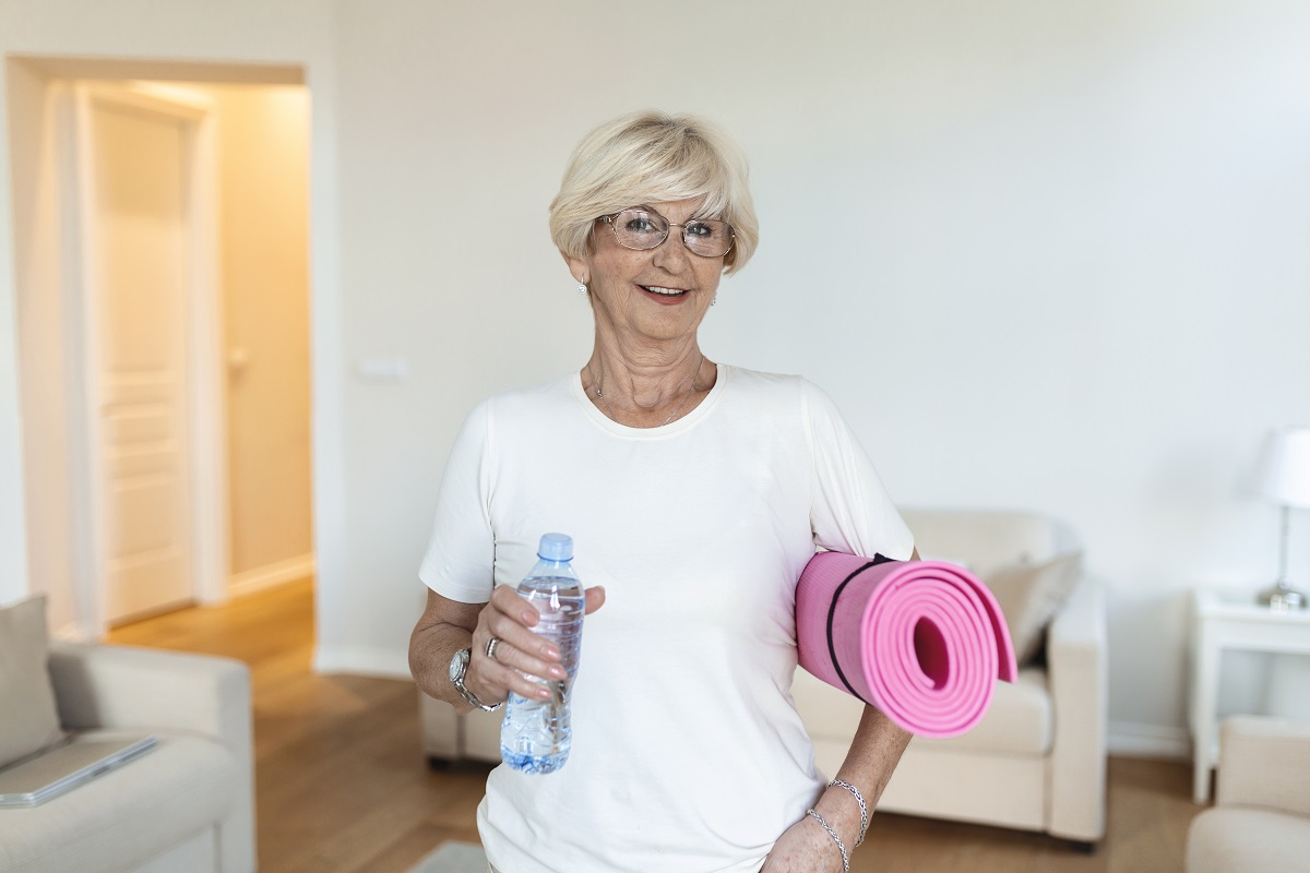 Mature Woman getting ready for a workout. Elderly woman ready for working out. Refreshment after training. Sporty old woman drinking water